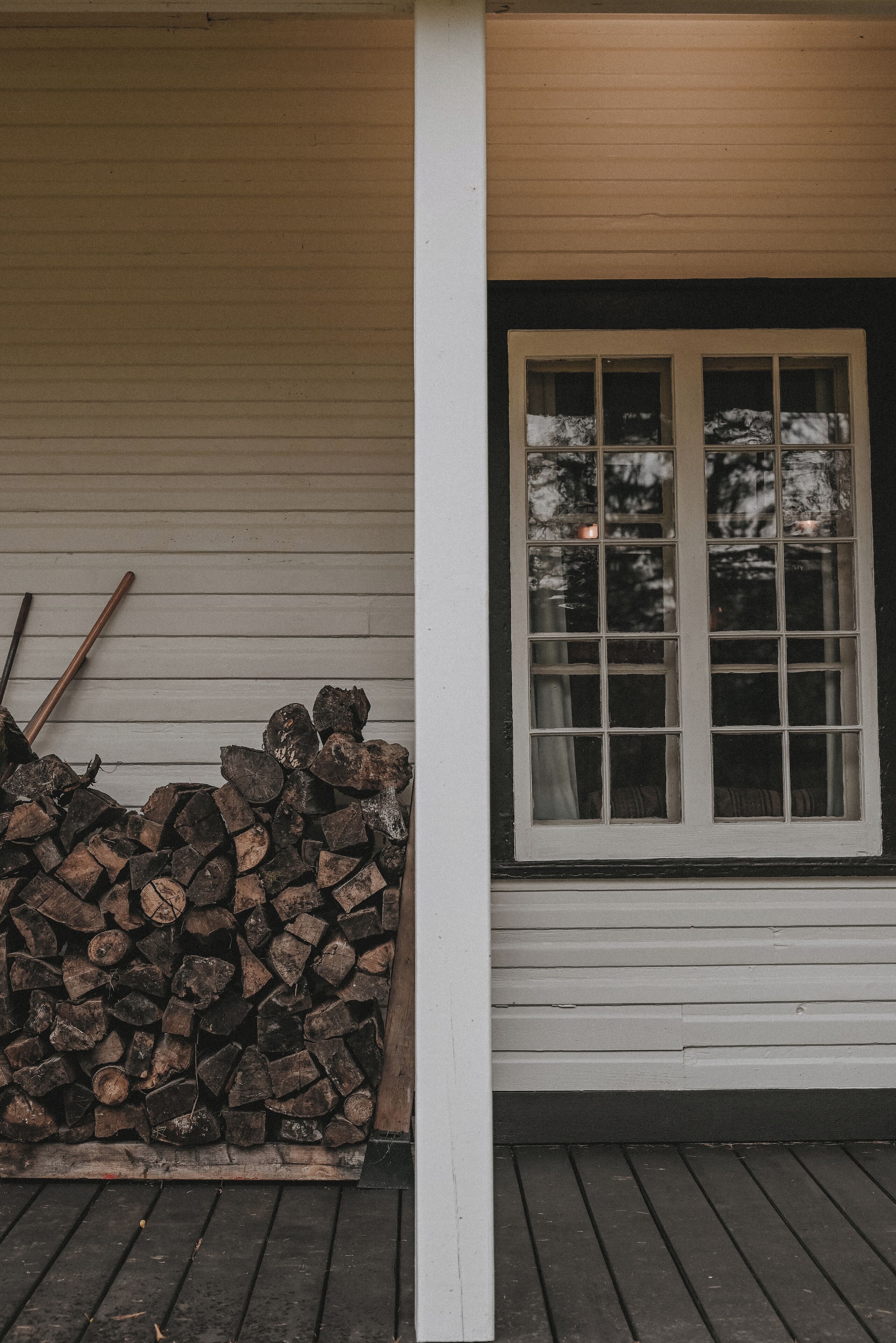 A wooden deck with a stack of firewood and a window with a view of trees.