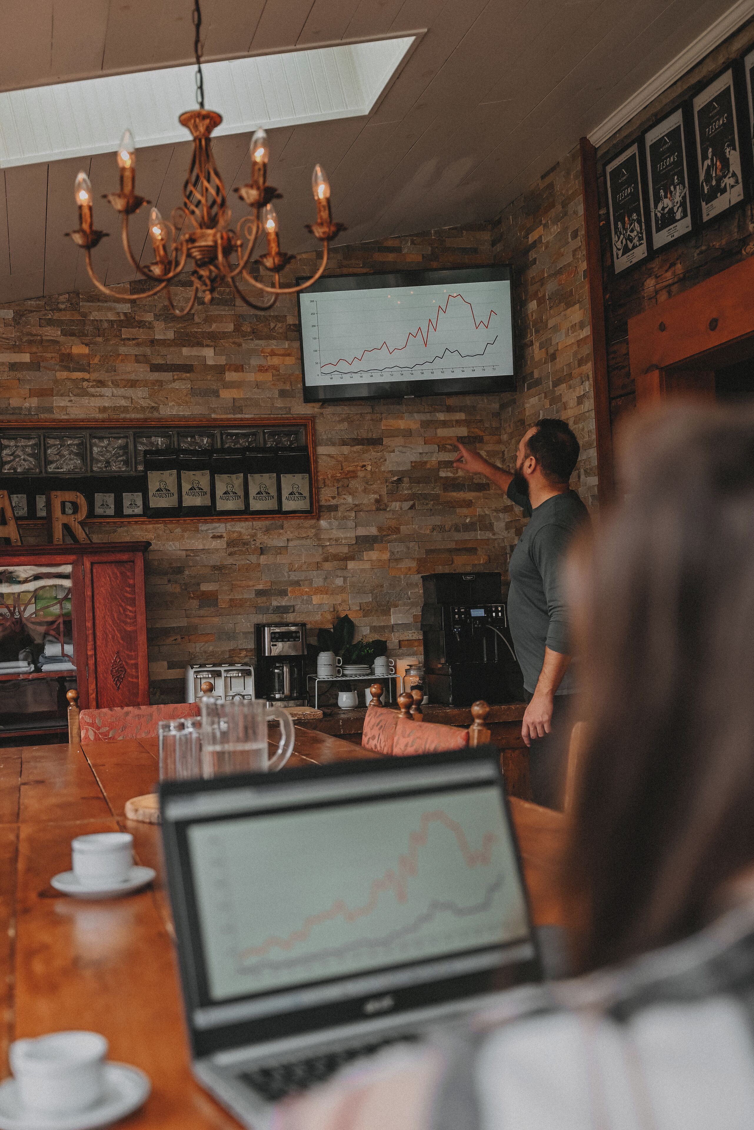 A bar area with a laptop displaying a graph, a coffee machine, and a television on the wall.