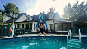 Una piscina con una persona che vi si tuffa, circondata da case e un'area patio coperta.