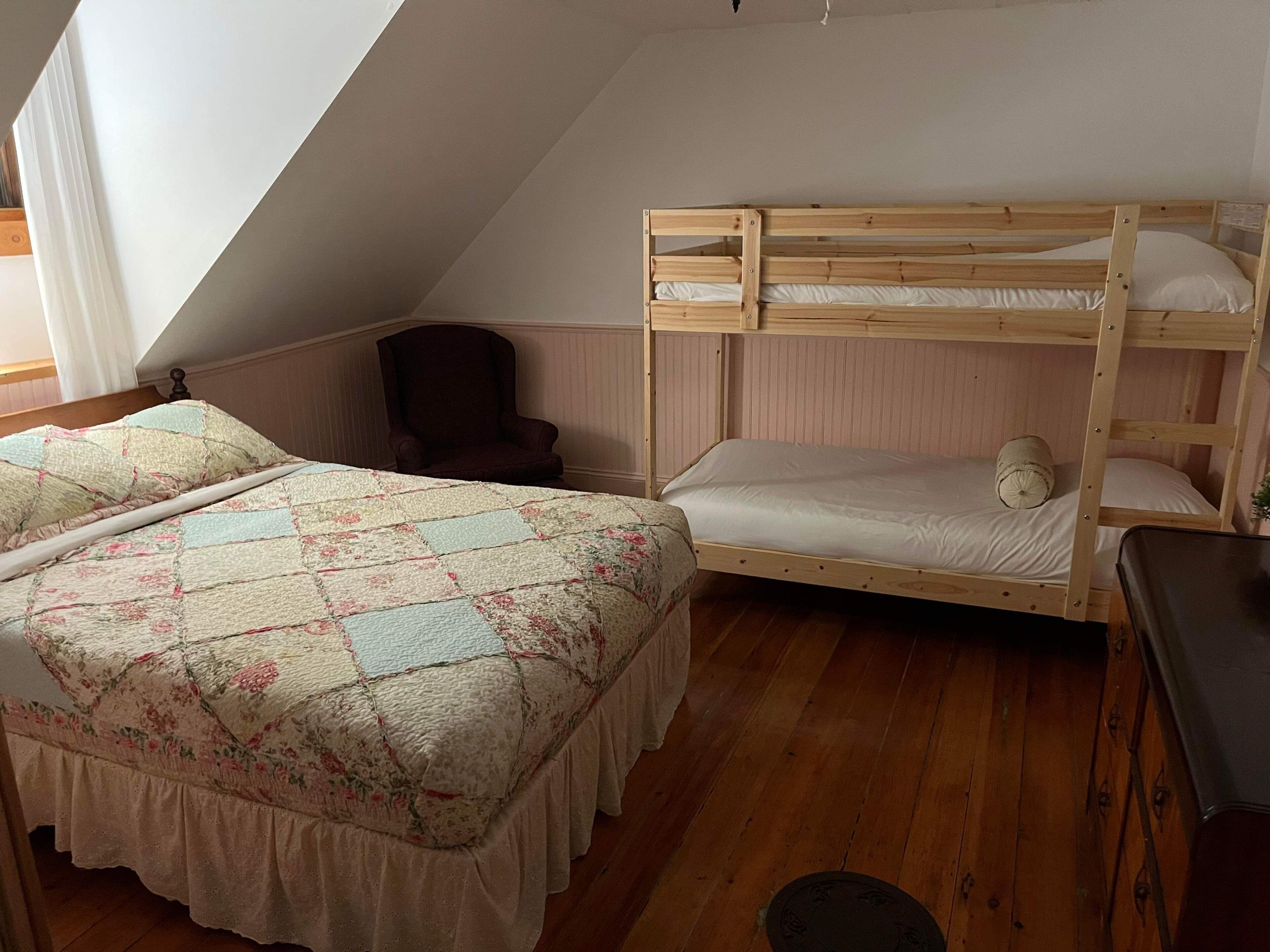 A dormitory room with two bunk beds, a chair, and a desk.