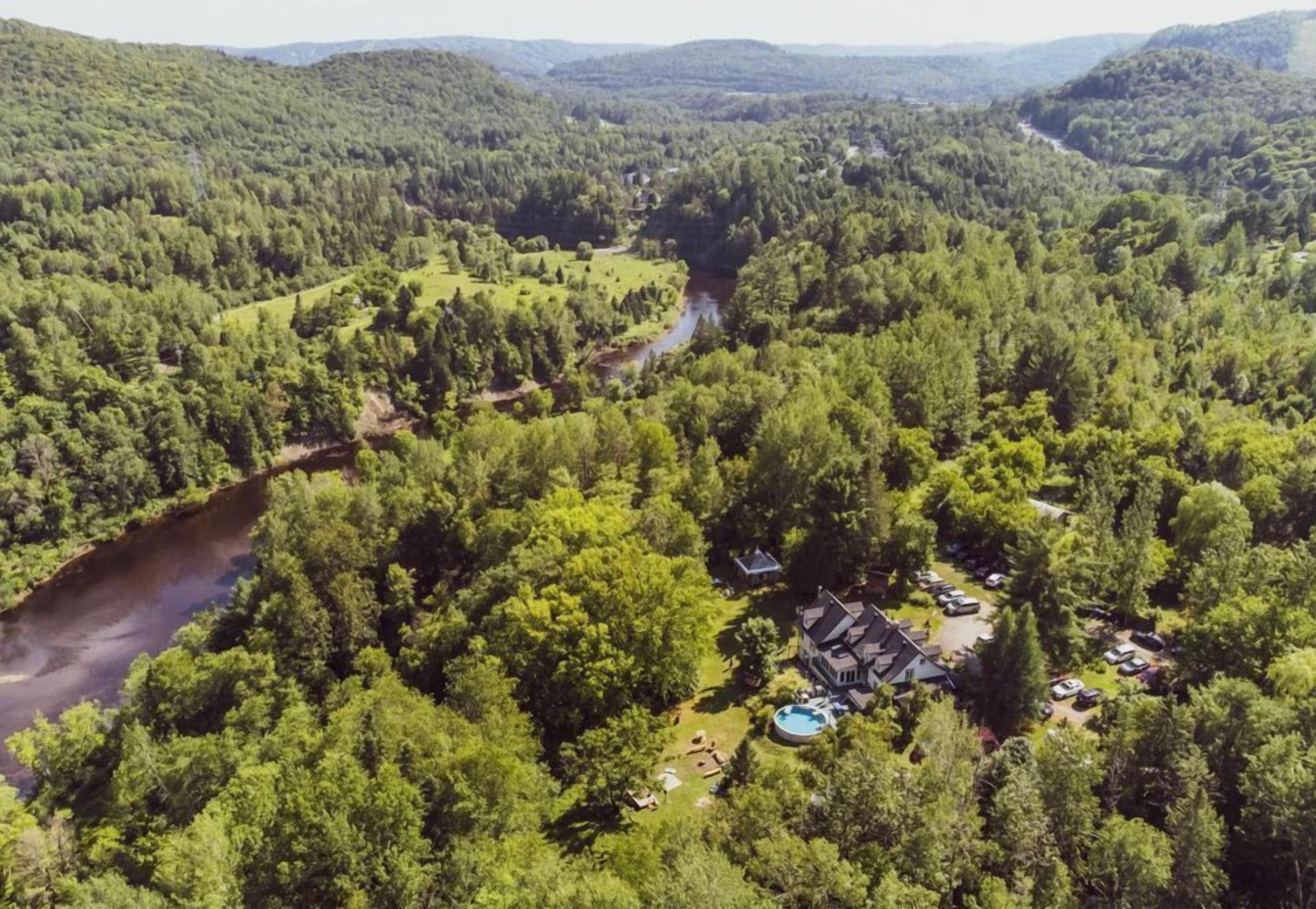 Una casa grande rodeada de un bosque frondoso, una piscina y un río.