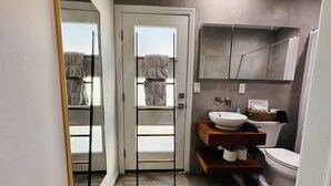 Een moderne badkamer met een glazen douchedeur, een wit wastafelmeubel, een toilet en een handdoekrek.