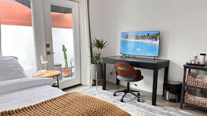 Een moderne hotelkamer met een bed, een bureau met een televisie, een potplant en een rieten mand.
