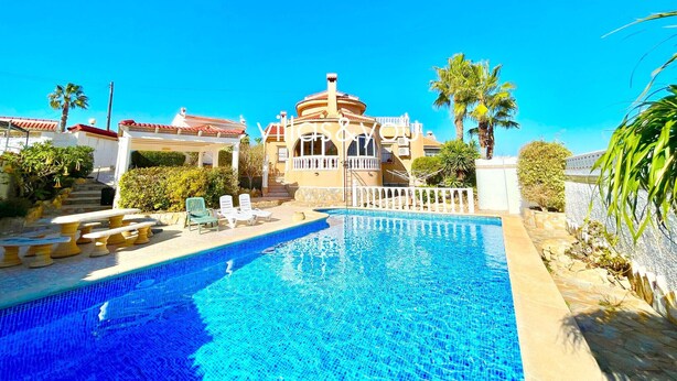 A swimming pool with a tiled deck, a covered seating area, and a building with a dome and arched windows.