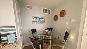 A dining area with a glass table and four chairs, a painting on the wall, and a small plant on the table. - Beachfront Condo on Mustang Padre Island (Corpus Christi)