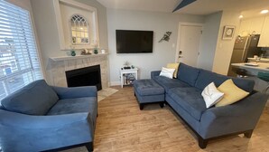 A living room with a fireplace, a television, and a kitchen area in the background. - Beachfront Condo on Mustang Padre Island (Corpus Christi)