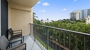A balcony with two wicker chairs, a railing, and a view of a cityscape with buildings and trees.