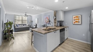 A modern kitchen with a central island, built-in appliances, and a dining area with a gray sofa and a ceiling fan.