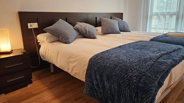 Ein Schlafzimmer mit Bett, Nachttisch, Lampe und einem Fenster.