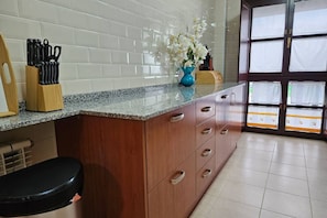 A kitchen with white tiled backsplash, a granite countertop, wooden cabinets, a black stool, and a window with blinds. - 13B01 Apartment with Garage and Terrace by R2R (Ribadesella)