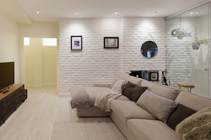 Una sala de estar moderna con una pared blanca con textura, un sofá, un televisor y cuadros enmarcados.