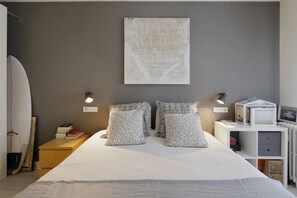 A bedroom with a bed, pillows, a surfboard, a bookshelf, and a wall-mounted artwork.