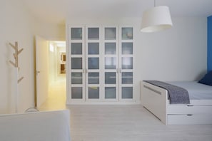 Un dormitorio con cama, un armario con puertas de cristal esmerilado, una lámpara colgante y una puerta que da a otra habitación.