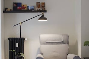 Una silla, una lámpara de pie, un radiador y una estantería con libros e imágenes.