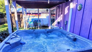 Un bain à remous installé à l’extérieur, avec une terrasse en bois et un mur violet.