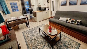 Un salon moderne avec un canapé, une table basse et une table à manger pour quatre personnes. On aperçoit une cuisine au fond.