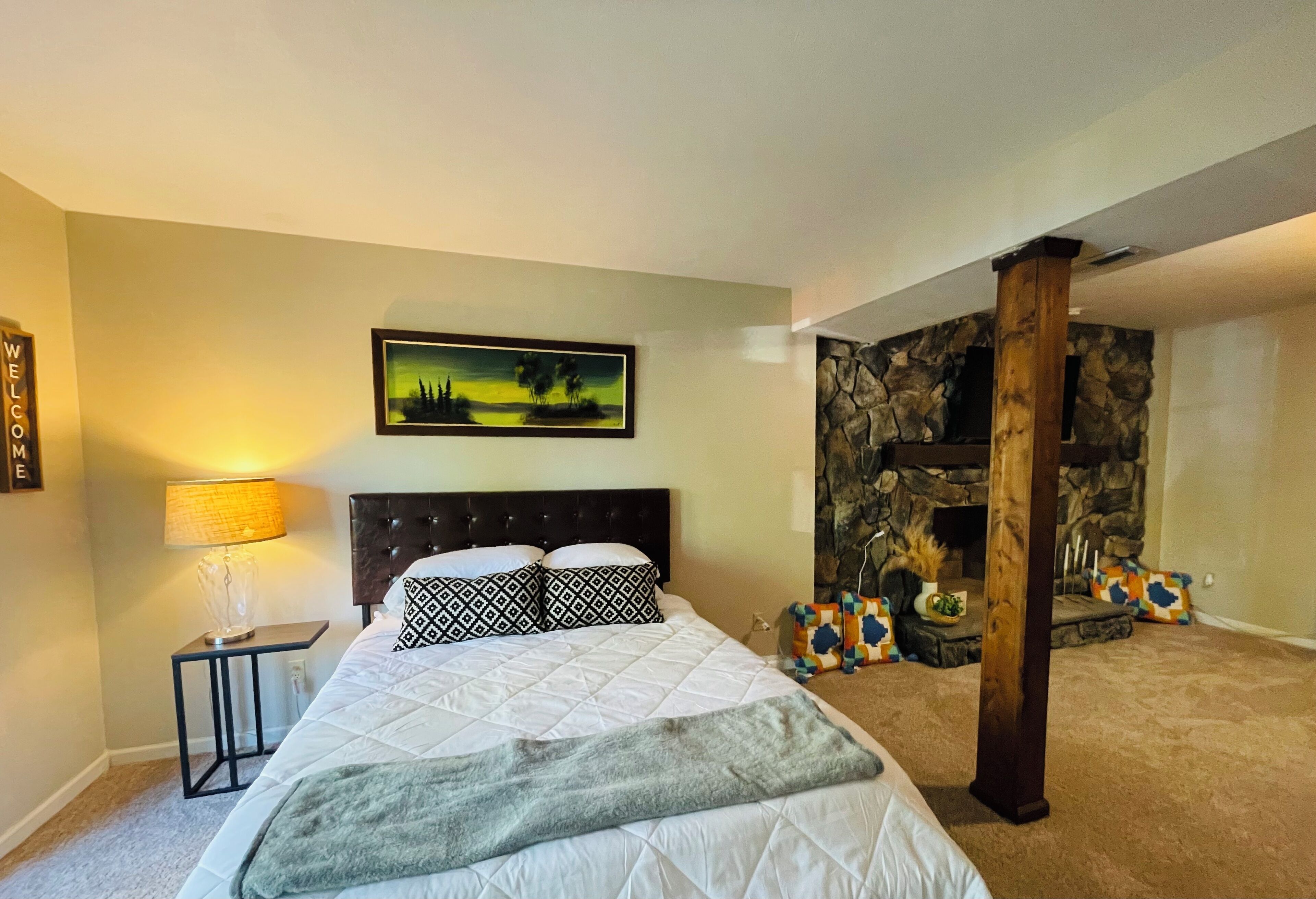 Un dormitorio con cama, mesita de noche, lámpara, cuadro, pared de piedra y pilar de madera.