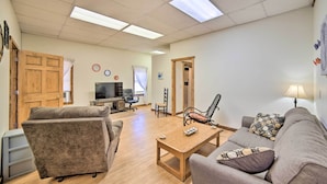 A spacious living room with a sofa, a coffee table, and a TV. There are wooden doors and a chair in the background. - 2 Mi to Ice Caves: Pet-friendly Eben Junction Apt (Eben Junction)