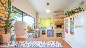 A compact kitchen with a brick wall, a window, and a hanging pot rack. - Local Paradisíaco NA Ilha DA Magia Loft Arcano Maior (Lagoa da Conceição Florianópolis)