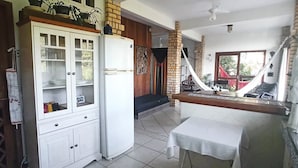A kitchen with a white refrigerator, a wooden cabinet, and a dining area with a table. - Local Paradisíaco NA Ilha DA Magia Loft Arcano Maior (Lagoa da Conceição Florianópolis)