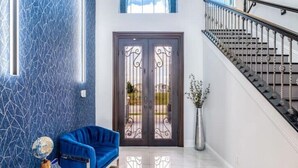 Een modern interieur met een blauwe, patroonrijke muur, een blauwe bank, een dubbele deur met decoratieve ijzerwerk en een trap met een metalen leuning.