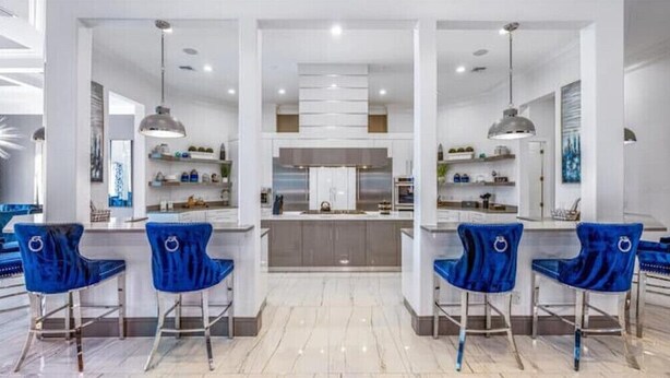Een moderne keuken met een centraal eiland, een bar met blauwe fluweelstoelen en hanglampen.