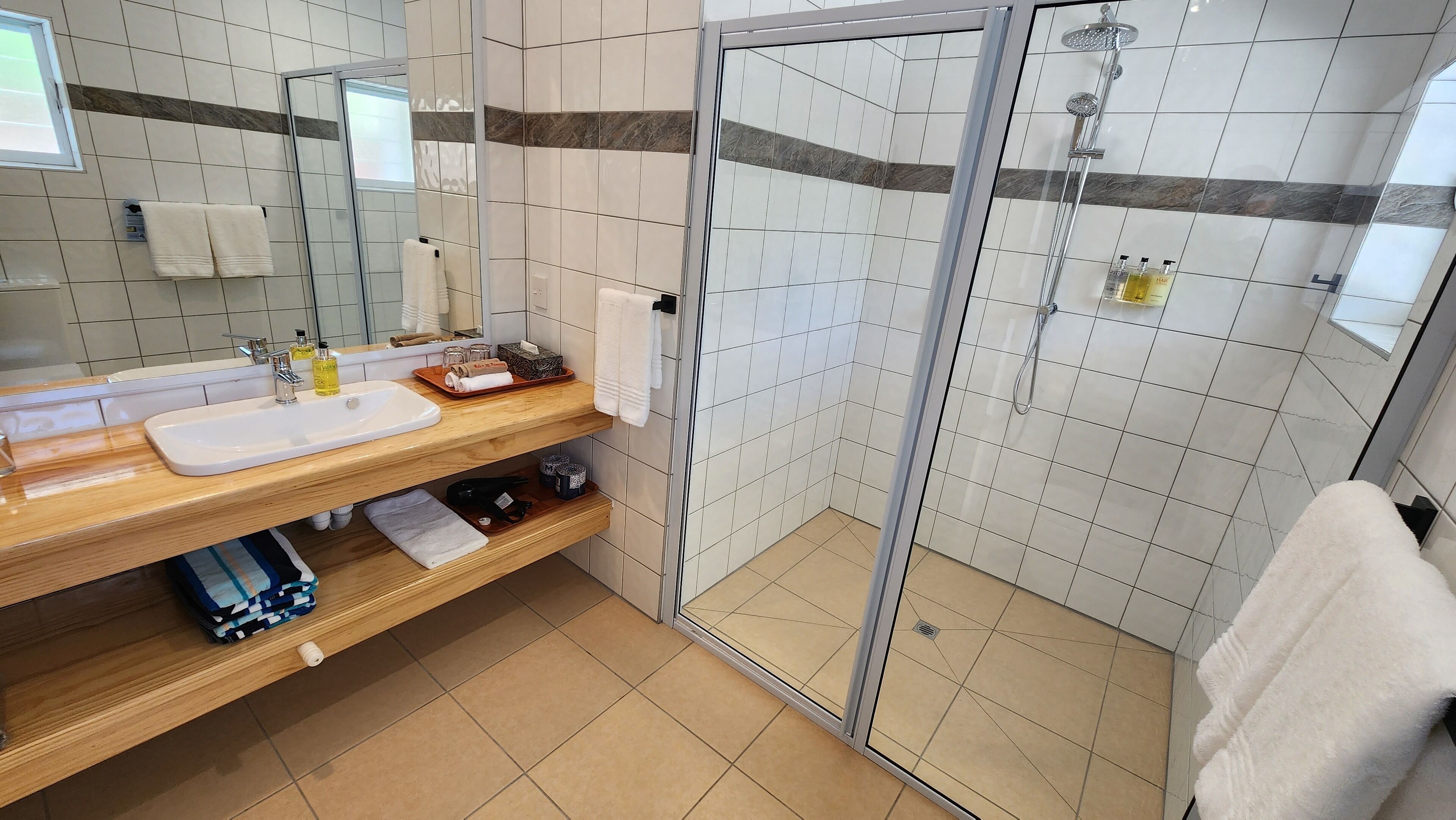 Een moderne badkamer met een glazen douchecabine, een houten wastafelmeubel en een spiegel.