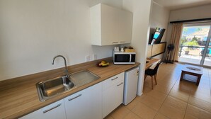A modern kitchen with a stainless steel sink, white cabinets, a microwave, and a small refrigerator. - Resort Tava'e (Aitutaki)