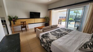 A modern hotel room with a bed, a TV, a desk, and a view of the outdoor area. - Resort Tava'e (Aitutaki)