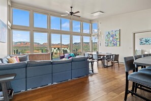 Un amplio espacio de sala con un sofá seccional grande, una mesa de comedor y sillas. Hay ventanas grandes que ofrecen vistas a formaciones rocosas rojas.