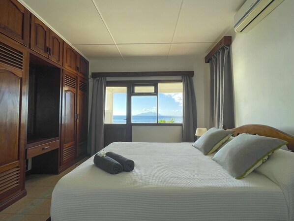 Una habitación de hotel con cama, armario, ventana con vista al mar y aire acondicionado.