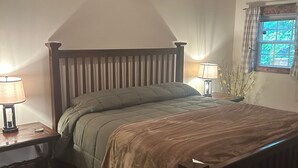 A bedroom with a wooden bed, two bedside tables with lamps, a window with curtains, and a wooden floor. - Family size Barndo,  Side by Side friendly......Lots of Trails to explore. (Sunbright)