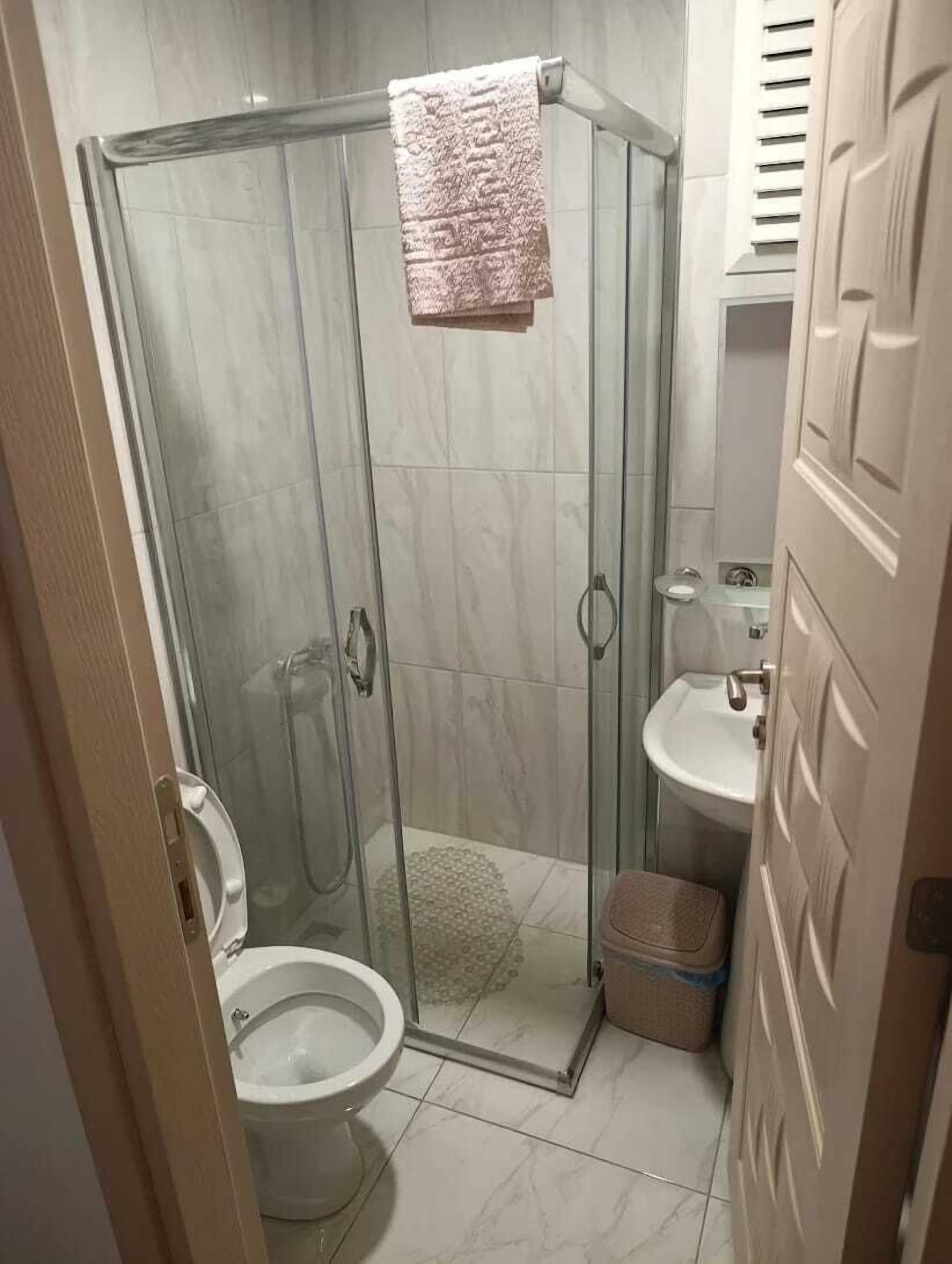 A bathroom with a glass shower enclosure, a toilet, a sink, and a towel hanging on the shower door.