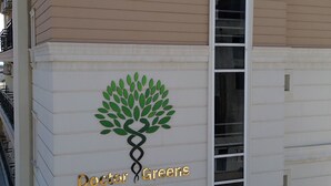 Un edifici amb façana beix i blanca, un logotip amb un arbre i el text "Doctor Greens", i una finestra vertical.