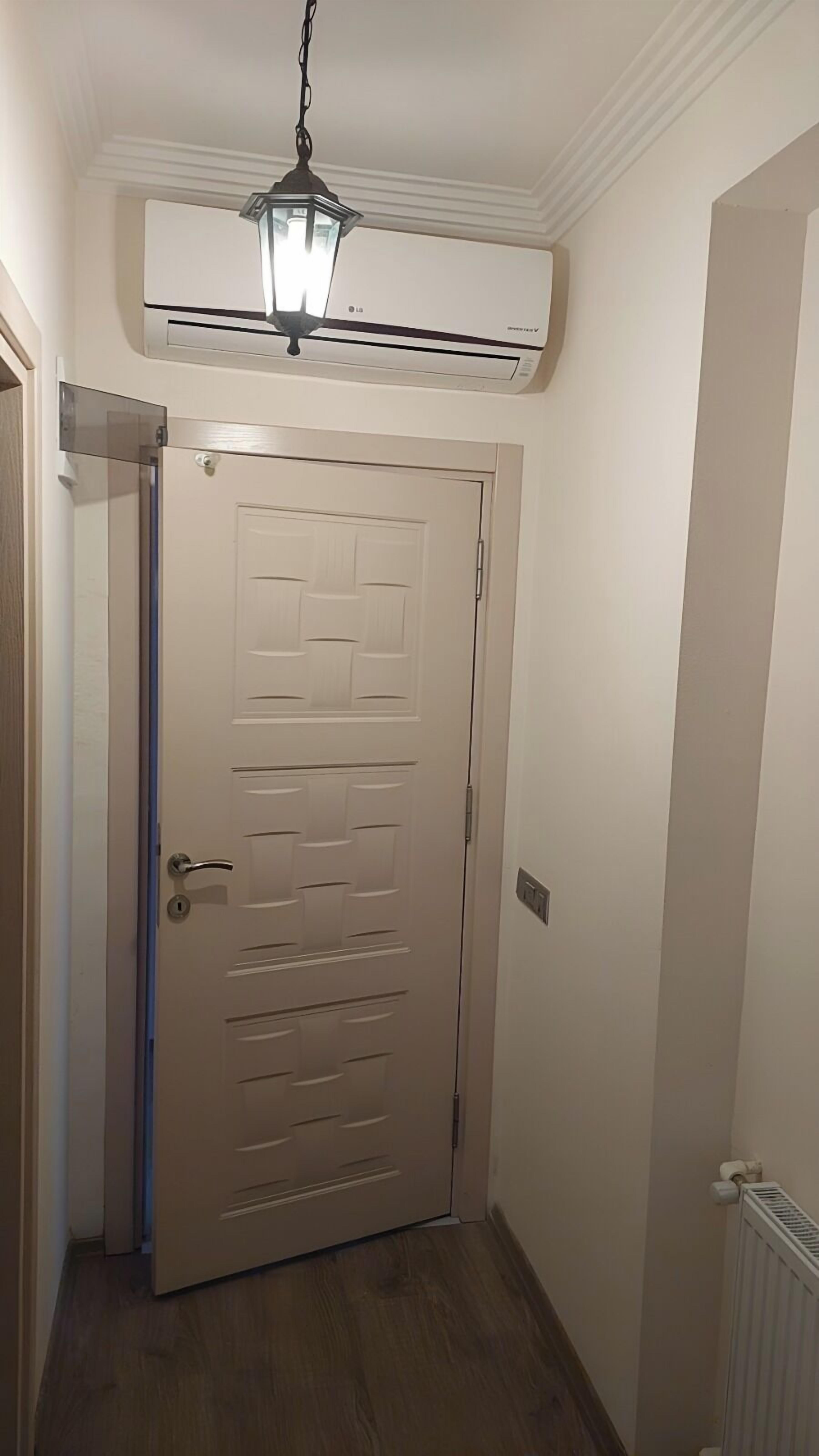 Un couloir avec une porte blanche, un appareil de climatisation et un luminaire.