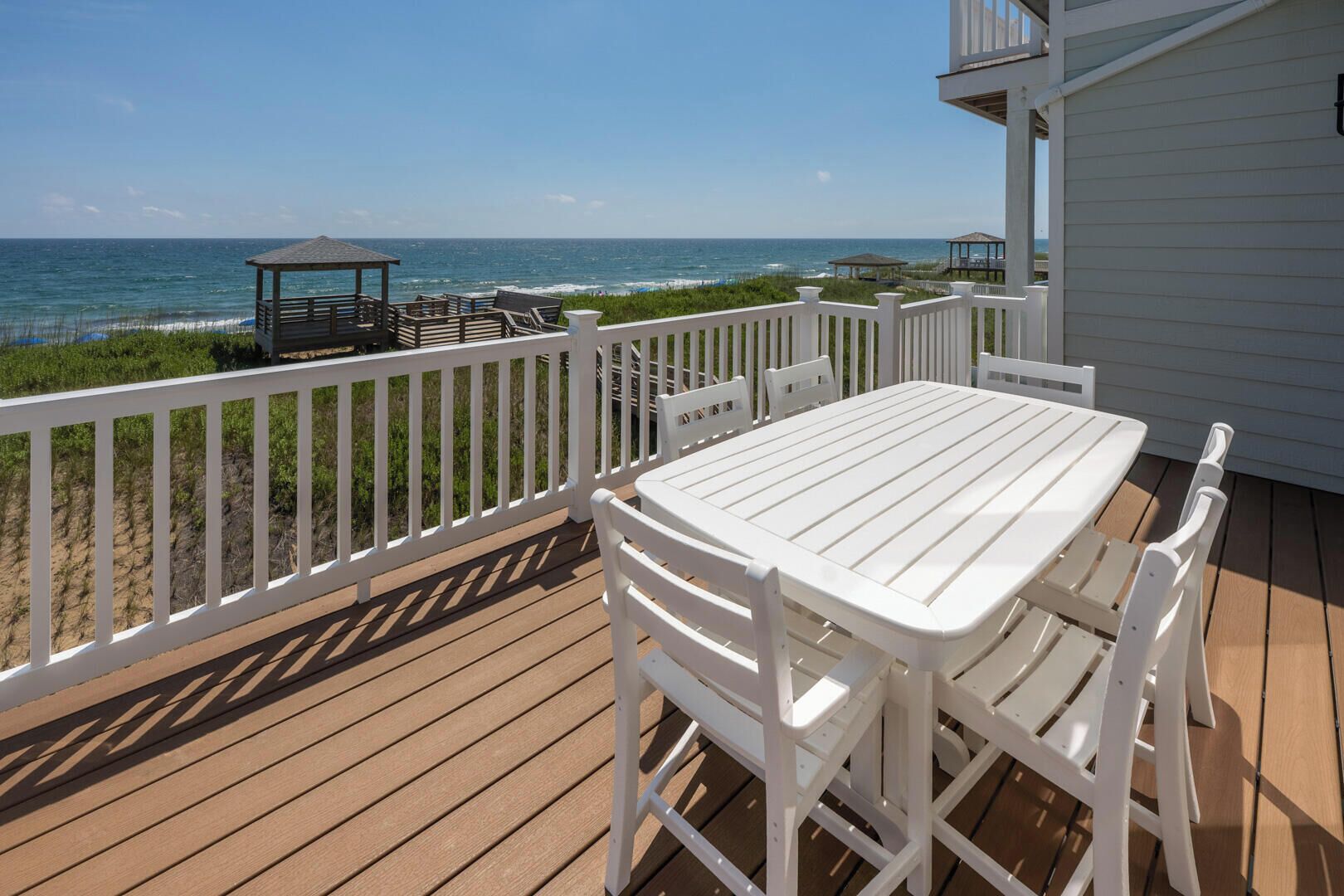 A wooden deck with a white table and chairs, overlooking the ocean.