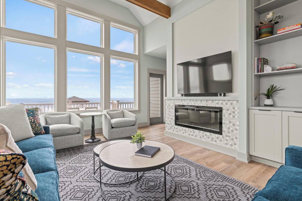 A spacious living room with a large TV, comfortable seating, a fireplace, and a view of the ocean.