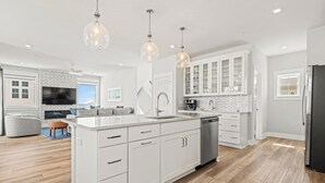A modern kitchen with white cabinetry, a central island, and pendant lighting. - The Tides by KEES Vacations (Kill Devil Hills)