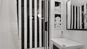 Un baño moderno con un box de ducha a rayas negras y blancas, un lavamanos blanco y un espejo sobre él.