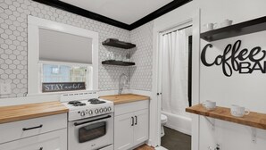 Una cocina moderna con armarios blancos, encimera de madera y estufa. Hay estantes sobre el lavamanos y un letrero en la pared que dice 'Coffee Bar'.