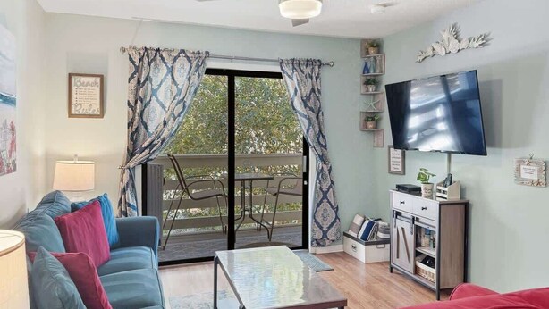 Ein Wohnzimmer mit einer Couch, einem Couchtisch, einem Fernseher und einer Glasschiebetür, die zu einem Außenbereich führt.