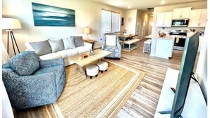 Ein modernes Wohnzimmer mit Sofa, Sessel, Couchtisch und einem Essbereich mit Tisch und Stühlen.