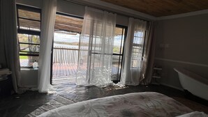Ein Schlafzimmer mit einem großen Bett, einer Holzbalkendecke und Blick auf einen Balkon mit Geländer.
