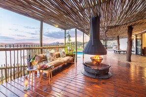 Une terrasse en bois avec un canapé, une table avec des boissons et un foyer.