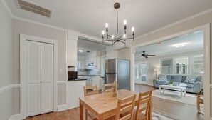 Una cocina moderna con armarios blancos, un refrigerador de acero inoxidable y un comedor con una mesa y sillas de madera.