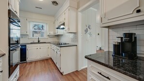 Una cocina moderna con armarios blancos, horno empotrado, cafetera y ventana con persianas.