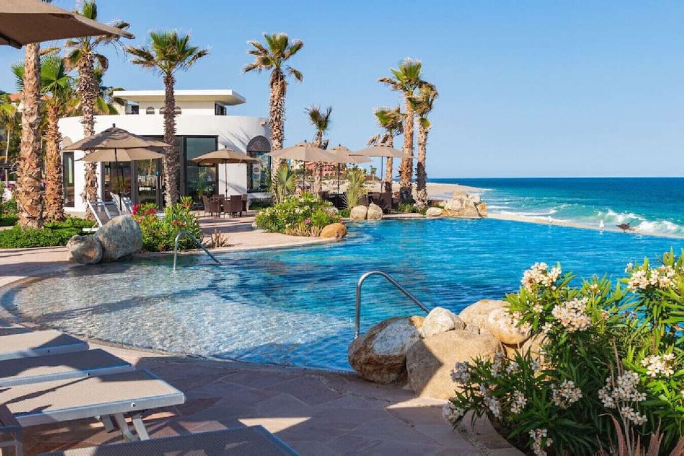 A resort pool with clear blue water, surrounded by palm trees and a view of the ocean.