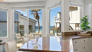 A spacious room with a large window overlooking the beach, a dining area with chairs, and a kitchen with cabinets. - The Mission Beach VIP- Luxury Home, 3 Private Decks, 30 steps to the Beach!  (San Diego)