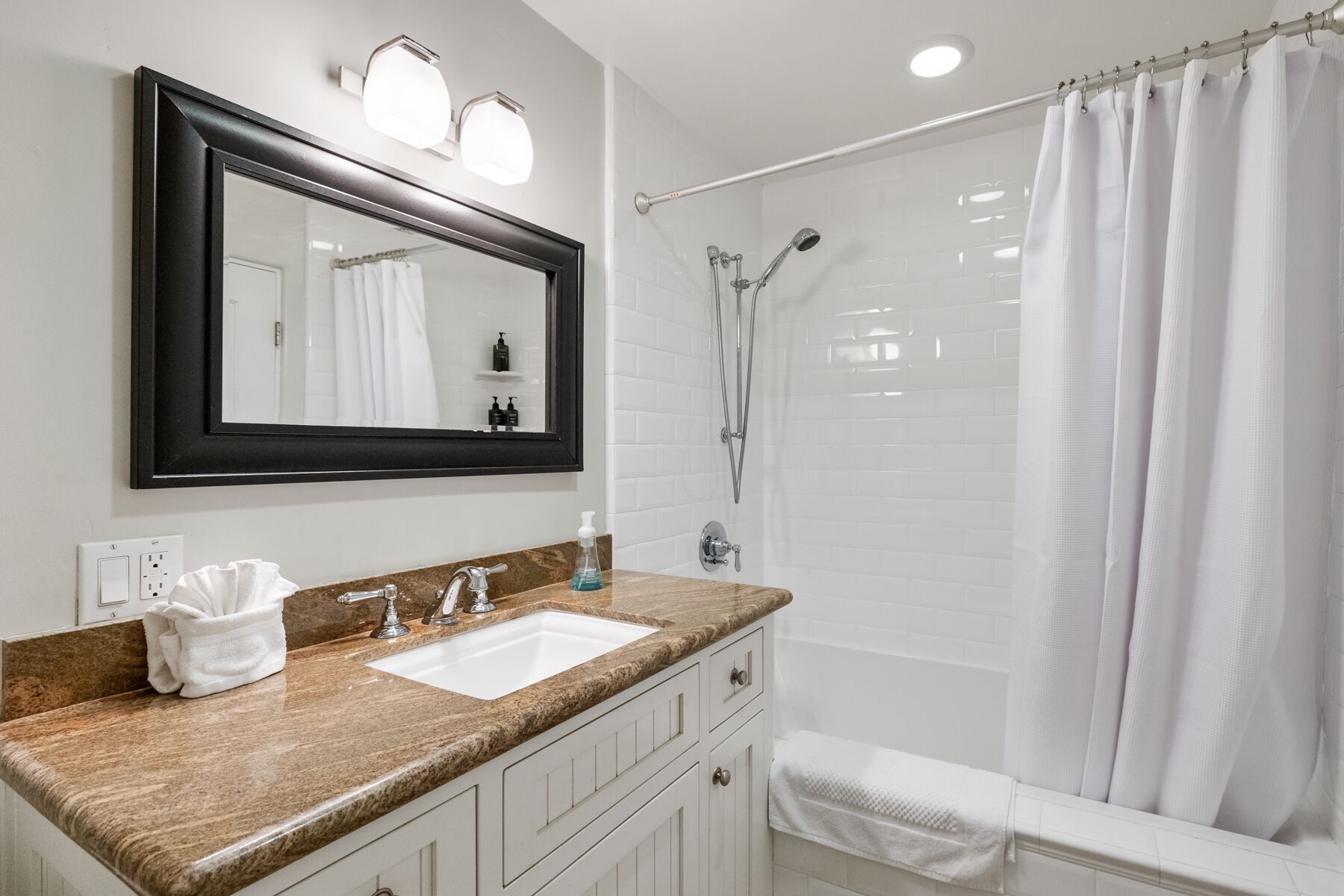 A bathroom with a sink, mirror, shower, and towel rack.
