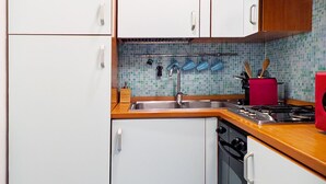 Una cocina con armarios blancos, un salpicadero azulejado, encimera de madera, estufa y fregadero.